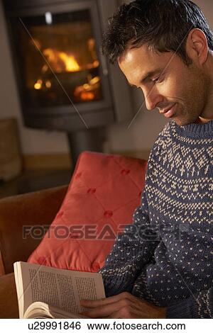 Stock Photograph - Middle Aged Man Relaxing With Book By Cosy Log Fire. Fotosearch