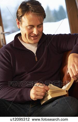 Stock Image - Middle Aged Man Relaxing With Book Sitting On Sofa. Fotosearch