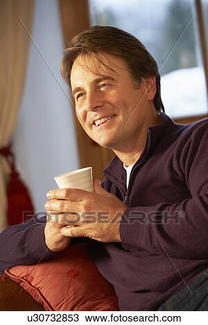 Middle Aged Man Relaxing With Hot Drink On Sofa Watching TV View Large Photo Image Stock Image - Middle Aged Man Relaxing With Hot Drink On Sofa Watching TV. Fotosearch