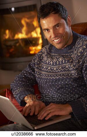 Stock Photograph - Middle Aged Man Using Laptop Computer By Cosy Log Fire. Fotosearch