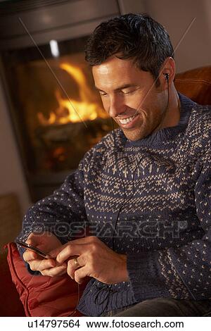 Picture - Middle Aged Man Using MP3 Player By Cosy Log Fire. Fotosearch
