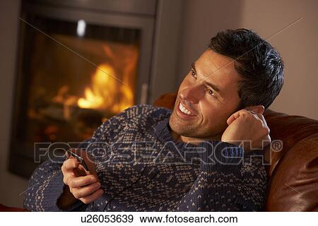 Stock Photo - Middle Aged Man Using MP3 Player By Cosy Log Fire. Fotosearch