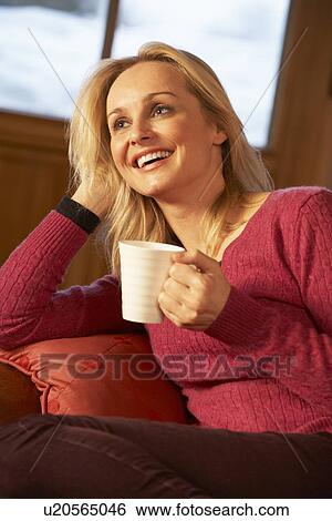 Stock Photograph - Middle Aged Woman Relaxing With Hot Drink On Sofa Watching TV. Fotosearch