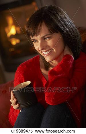 Stock Photography - Middle Aged Woman Relaxing With Hot Drink By Cosy Log Fire. Fotosearch