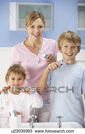 Stock Image - Mother and children cleaning teeth in bathroom. Fotosearch