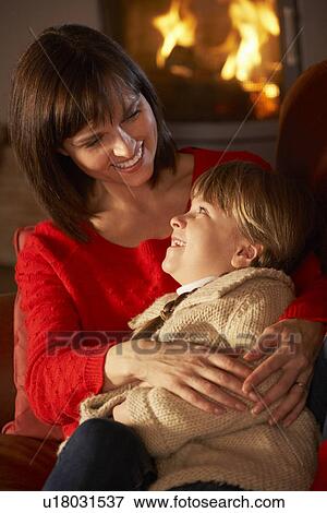 Stock Photo - Mother And Daughter Relaxing On Sofa By Cosy Log Fire. Fotosearch