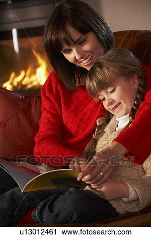Mother And Daughter Sitting On Sofa And Reading Book By Cosy Log Fire View Large Photo Image Stock Image - Mother And Daughter Sitting On Sofa And Reading Book By Cosy Log Fire. Fotosearch