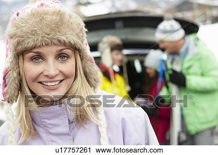 Stock Image - Mother Smiling At Camera Whilst Family Load Skis In Boot Of Car. Fotosearch