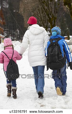 Stock Image - Mother Walking Two Children To School Along Snowy Street In Ski Resort. Fotosearch
