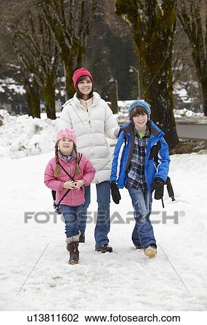 Stock Image - Mother Walking Two Children To School Along Snowy Street In Ski Resort. Fotosearch