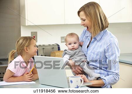 Stock Photograph - Mother with children using laptop in kitchen. Fotosearch