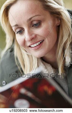 Stock Image - Outdoor Portrait Of Woman Wearing Winter Clothes Reading Magazine. Fotosearch