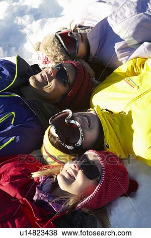 Stock Photo - Overhead View Of Teenage Family Lying In Snow On Ski Holiday In Mountains. Fotosearch