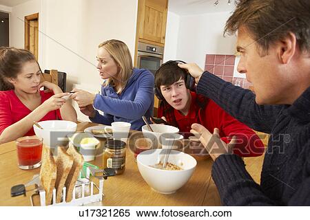 Stock Photography - Parents Taking Away Gadgets From Children Whilst Eating Breakfast Together In Kitchen. Fotosearch