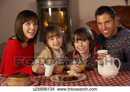 Picture - Portrait Of Family Enjoying Tea And Cake By Cosy Log Fire. Fotosearch