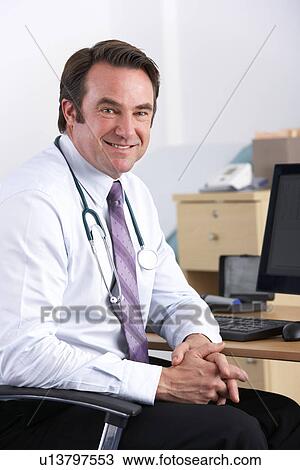 Stock Image - Portrait UK doctor sitting at desk. Fotosearch