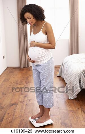 Stock Image - Pregnant woman weighing herself. Fotosearch