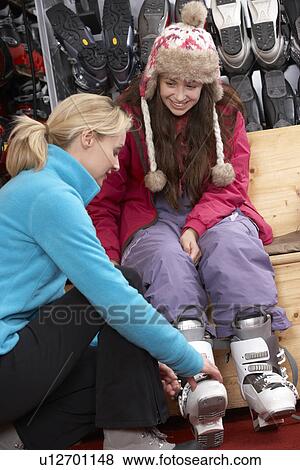 Stock Photo - Sales Assistant Helping Teenage Girl To Try On Ski Boots In Hire Shop. Fotosearch