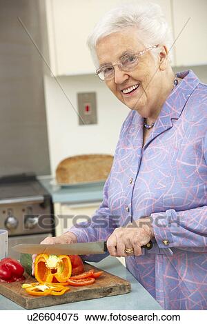 Stock Photography - Senior woman chopping vegetables in domestic kitchen. Fotosearch