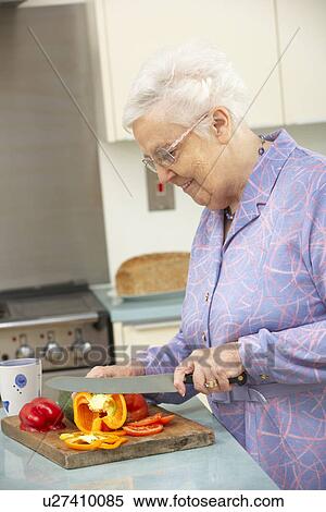 Stock Photography - Senior woman chopping vegetables in domestic kitchen. Fotosearch