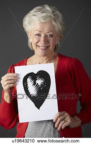 Stock Image - Senior woman holding ink drawing of heart. Fotosearch