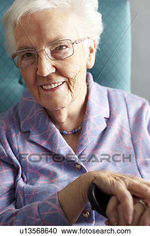 Stock Image - Senior Woman Relaxing In Chair Holding Walking Stick. Fotosearch