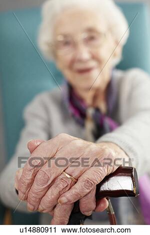 Stock Image - Senior Woman Relaxing In Chair Holding Walking Stick. Fotosearch