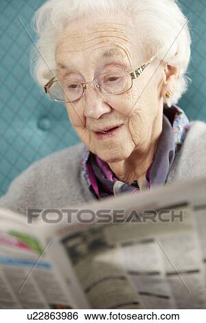 Stock Photograph - Senior Woman Relaxing In Chair Reading Newspaper. Fotosearch