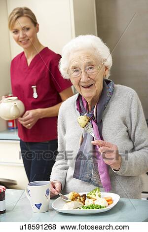 Stock Photo - Senior woman with carer eating meal at home. Fotosearch