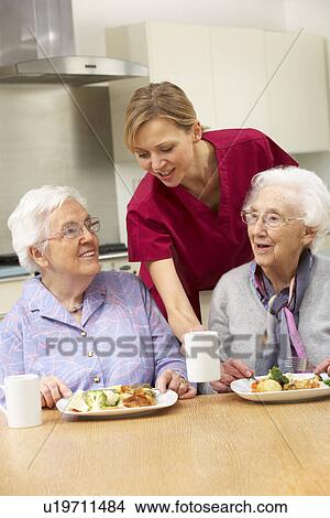 Picture - Senior women with carer enjoying meal at home. Fotosearch