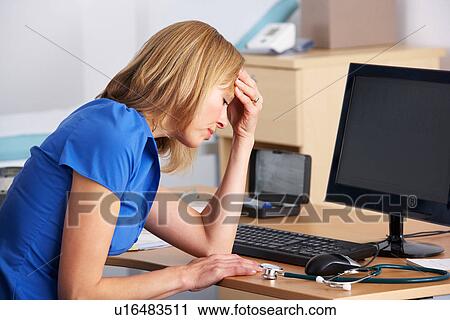 Stock Image - Stressed UK doctor sitting at desk. Fotosearch