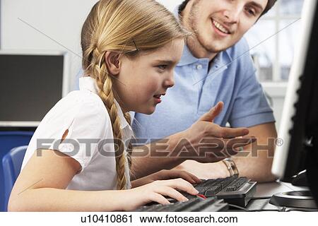 Stock Image - Teacher helping girl using computer in class. Fotosearch