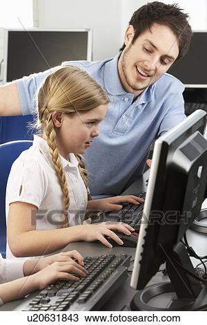 Stock Image - Teacher helping girl using computer in class. Fotosearch