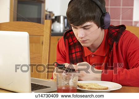 Teenage Boy Using Laptop And Listening To MP3 Player Whilst Eating Breakfast View Large Photo Image Stock Photo - Teenage Boy Using Laptop And Listening To MP3 Player Whilst Eating Breakfast. Fotosearch
