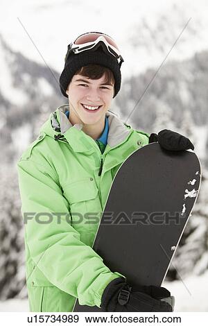 Stock Photo - Teenage Boy With Snowboard On Ski Holiday In Mountains. Fotosearch