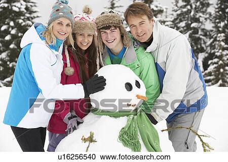 Stock Image - Teenage Family Building Snowman On Ski Holiday In Mountains. Fotosearch