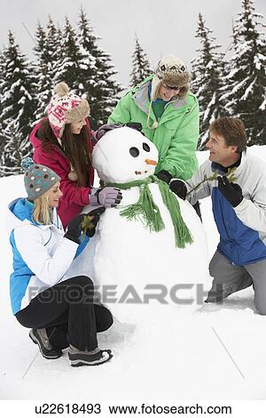 Stock Image - Teenage Family Building Snowman On Ski Holiday In Mountains. Fotosearch