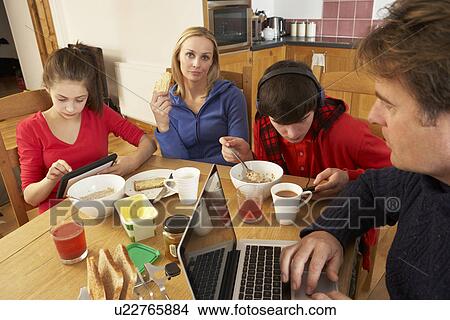 Picture - Teenage Family Using Gadgets Whilst Eating Breakfast Together In Kitchen. Fotosearch