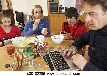 Teenage Family Using Gadgets Whilst Eating Breakfast Together In Kitchen View Large Photo Image Stock Photography - Teenage Family Using Gadgets Whilst Eating Breakfast Together In Kitchen. Fotosearch