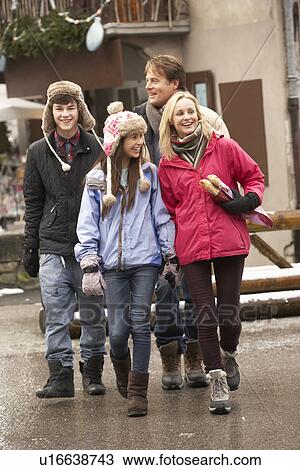 Stock Image - Teenage Family Walking Along Snowy Town Street In Ski Resort. Fotosearch