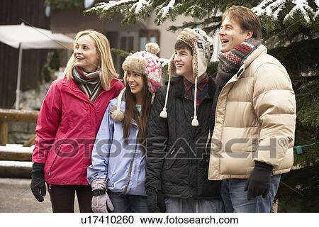 Stock Image - Teenage Family Walking Along Snowy Town Street In Ski Resort. Fotosearch