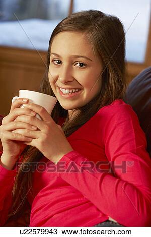Stock Image - Teenage Girl Relaxing On Sofa With Hot Drink. Fotosearch