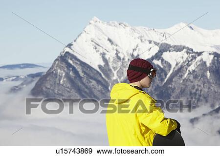Stock Photo - Teenage Snowboarder Admiring Mountain View Whilst On Ski Holiday In Mountains. Fotosearch