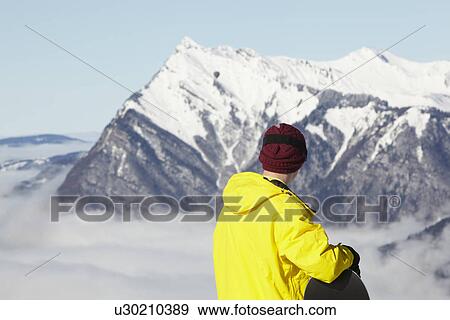 Stock Photo - Teenage Snowboarder Admiring Mountain View Whilst On Ski Holiday In Mountains. Fotosearch