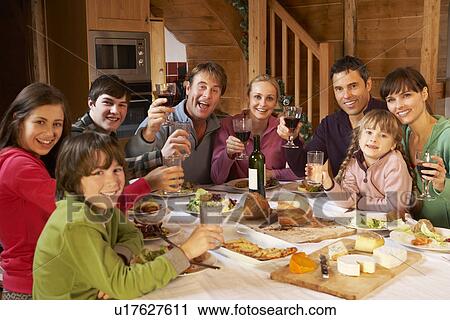 Stock Image - Two Familes Enjoying Meal In Alpine Chalet Together. Fotosearch