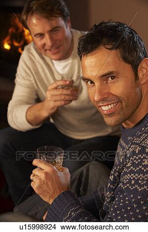 Picture - Two Middle Aged Men Relaxing Sitting On Sofa Drinking Whisky. Fotosearch