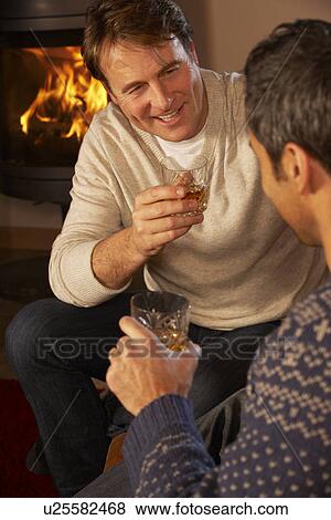 Stock Photo - Two Middle Aged Men Relaxing Sitting On Sofa Drinking Whisky. Fotosearch