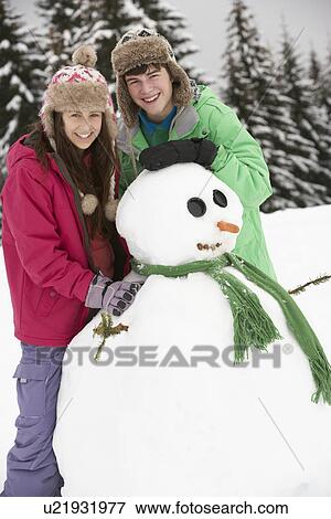 Stock Photo - Two Teenagers Building Snowman On Ski Holiday In Mountains. Fotosearch