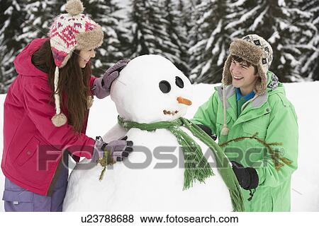 Stock Photo - Two Teenagers Building Snowman On Ski Holiday In Mountains. Fotosearch