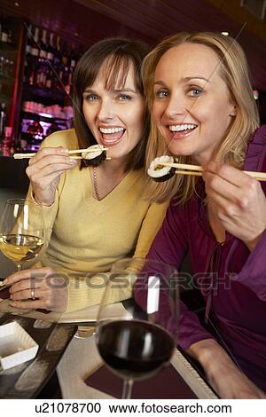 Stock Image - Two Women Enjoying Sushi In Restaurant. Fotosearch